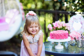 Most adorable little girl giggling in pink dress next to pink birthday cake Picture