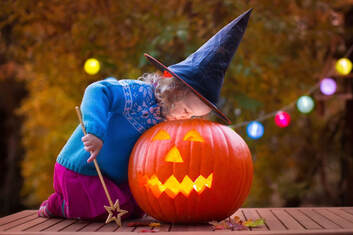 Adorable little tyke with witch's hat and fairy wand peering into lit pumpkin Picture