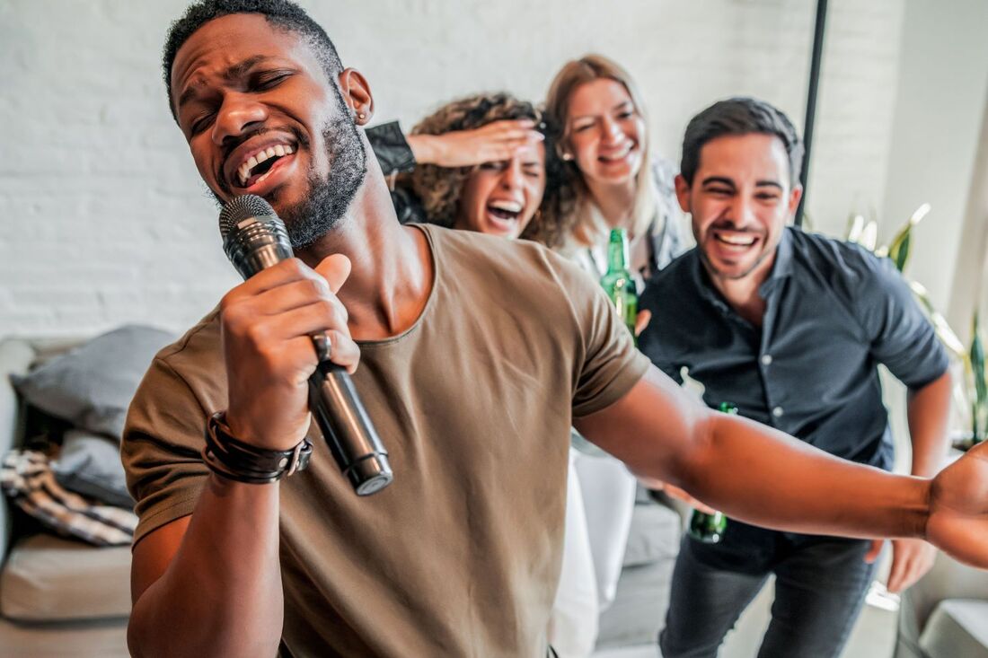 Man singing karaoke with gusto as his friends laugh hysterically in the background Picture